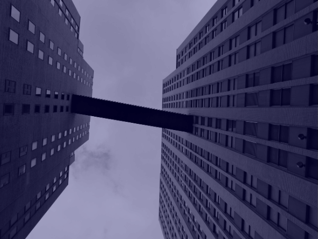 Vista de baixo entre dois prédios altos ligados por uma passarela, ilustrando conectividade corporativa como base de estabilidade e segurança na rede.
